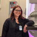 Vicki, a mammography technologist, stands next to a mammography machine