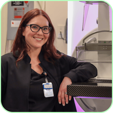 Vicki, a mammography tech, stands next to a mammogram machine